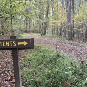 Gravel road in woods with “tents” sign pointing right